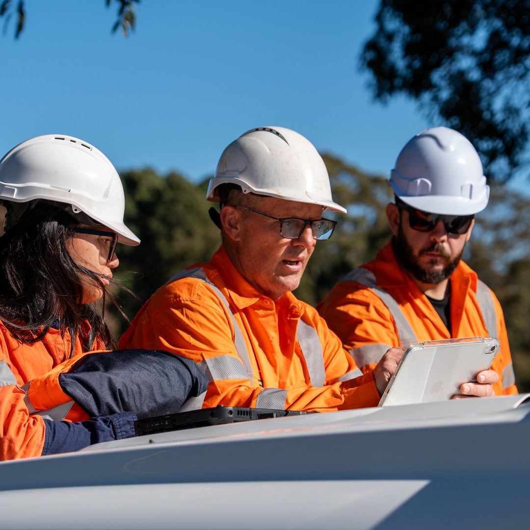 Three of the crew in hi-vis going over a tablet on the bonnet of a ute