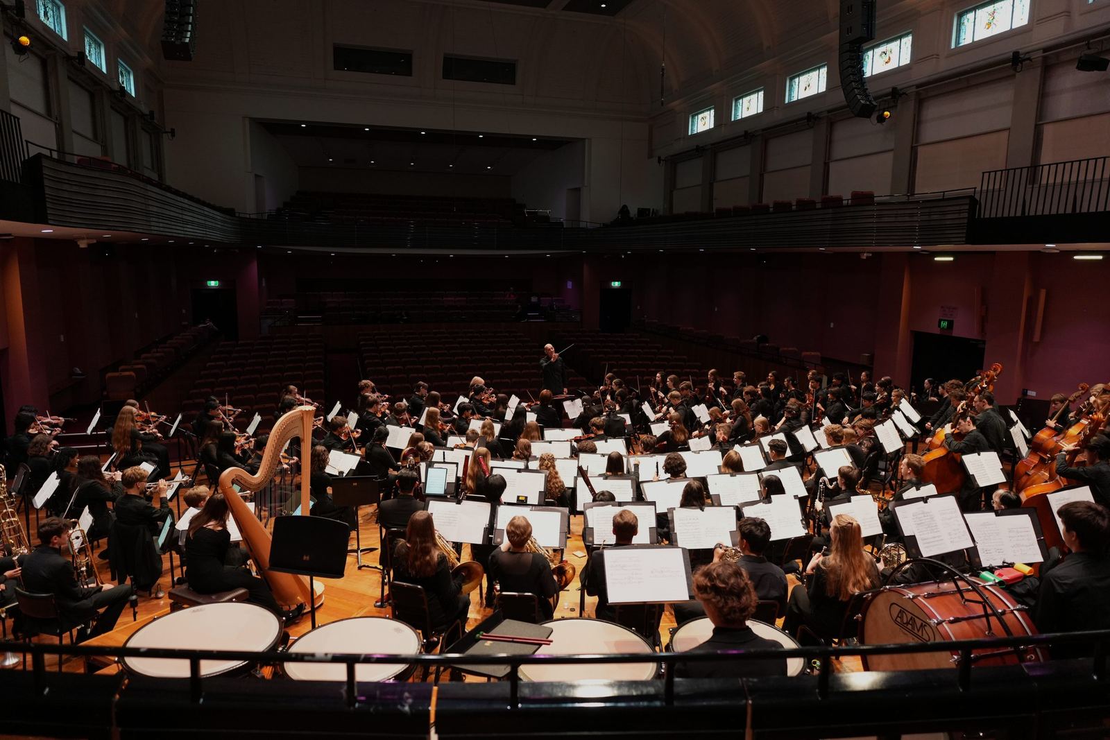 Youth orchestra rehearsing on a wide concert platform, seen from the stalls