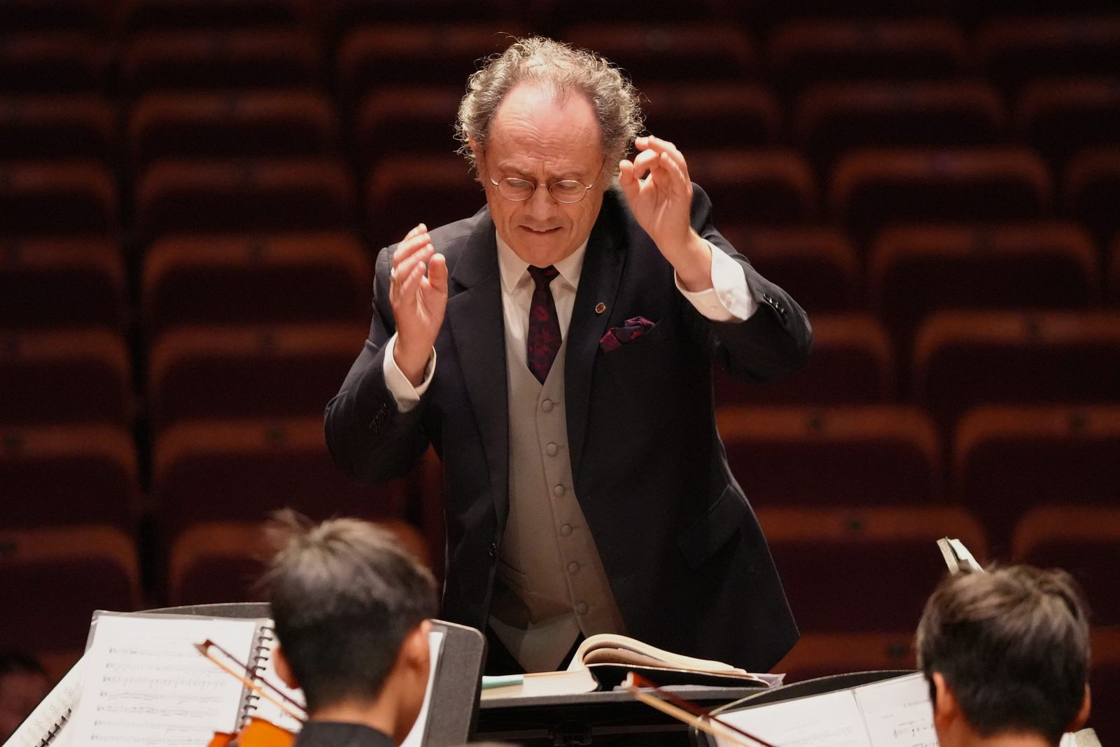 Conductor in a waistcoat leading the players, eyes down