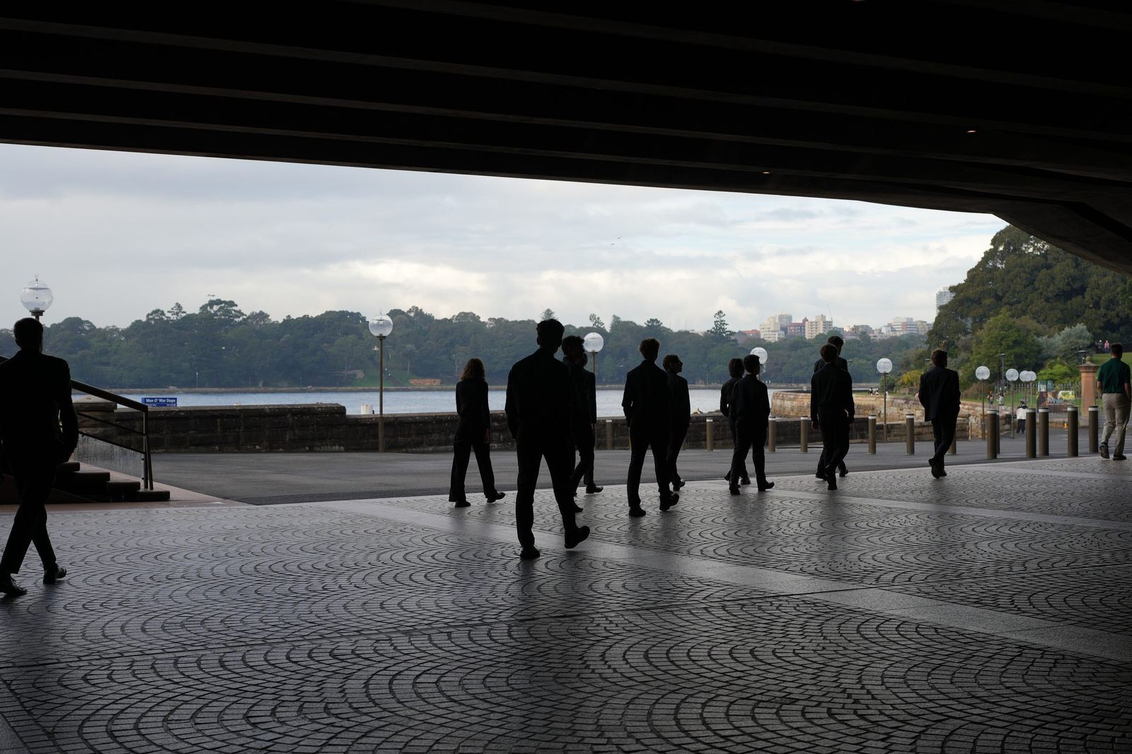 Musicians in silhouette walking under the Opera House