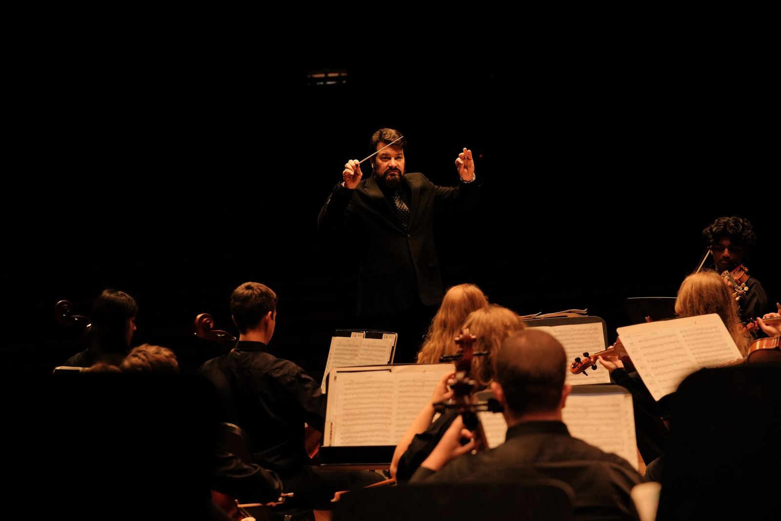 Conductor lit on a dark stage above the orchestra